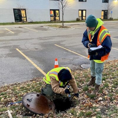 Two people inspecting a storm drain in parking lot area